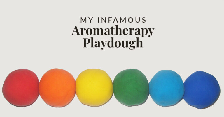 Six colorful balls of homemade playdough -red, orange, yellow, green, light blue, and dark blue - are lined up on a white surface beneath the text "My Infamous Aromatherapy Playdough," representing a vibrant, scent-infused DIY aromatherapy playdough recipe.