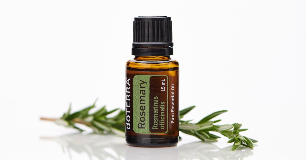 A 15 mL amber glass bottle of doTERRA Rosemary essential oil stands upright on a glossy white surface, flanked by fresh sprigs of rosemary. The label reads "Rosmarinus officinalis" and "Pure Essential Oil," highlighting its botanical source and purity.