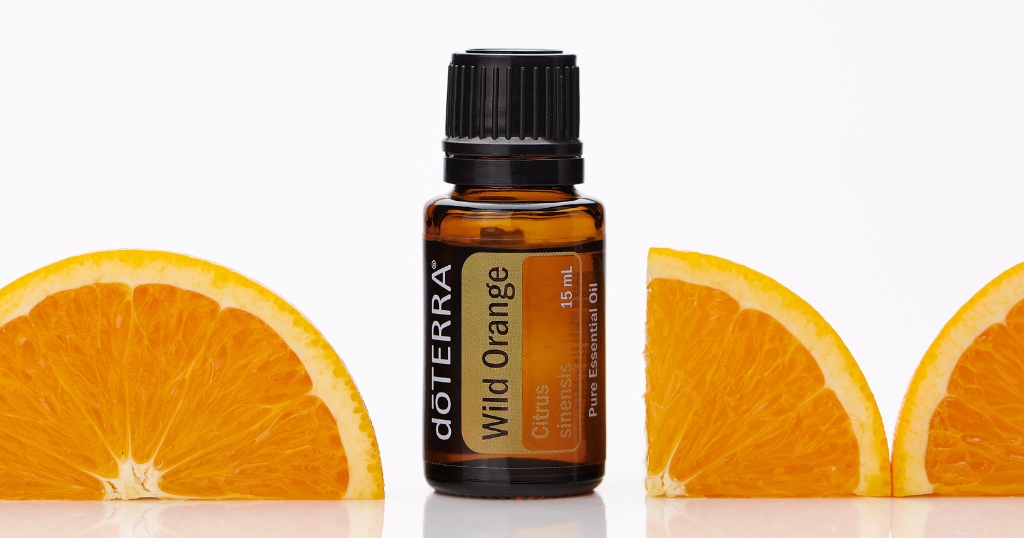 A 15 mL amber bottle of doTERRA Wild Orange essential oil stands upright, flanked by three vibrant orange slices on a reflective white surface. The label on the bottle reads "Citrus Sinensis" and "Pure Essential Oil," emphasizing its citrus source and purity.