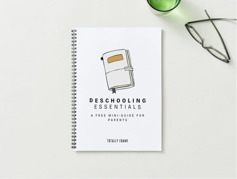A spiral-bound notebook titled “Deschooling Essentials: A Free Mini-Guide for Parents” lies on a white surface beside a pair of glasses and a green cup. The minimalist cover features an illustration of a closed journal. The image promotes a practical homeschooling resource for parents transitioning into deschooling.