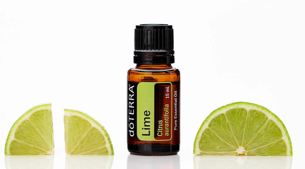 A bottle of doTERRA Lime essential oil labeled Citrus aurantifolia stands upright, flanked by fresh lime wedges on a white background. This bright citrus oil is a classic top note, often used in the 30-50-20 rule for blending essential oils to create balanced, aromatic DIY blends.