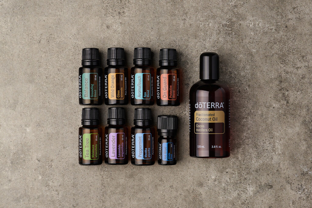 Flat lay of nine doTERRA essential oil bottles including Balance, Wild Orange, On Guard, Lavender, and Deep Blue, arranged next to a large bottle of fractionated coconut oil. This setup highlights popular carrier oils for beginners and essential oils commonly used for blending and topical application.