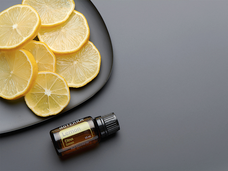 A doTERRA Lemon essential oil bottle rests beside a matte black plate topped with fresh lemon slices. This clean and vibrant setup visually answers “what are essential oils” by linking the oil directly to its natural citrus source.