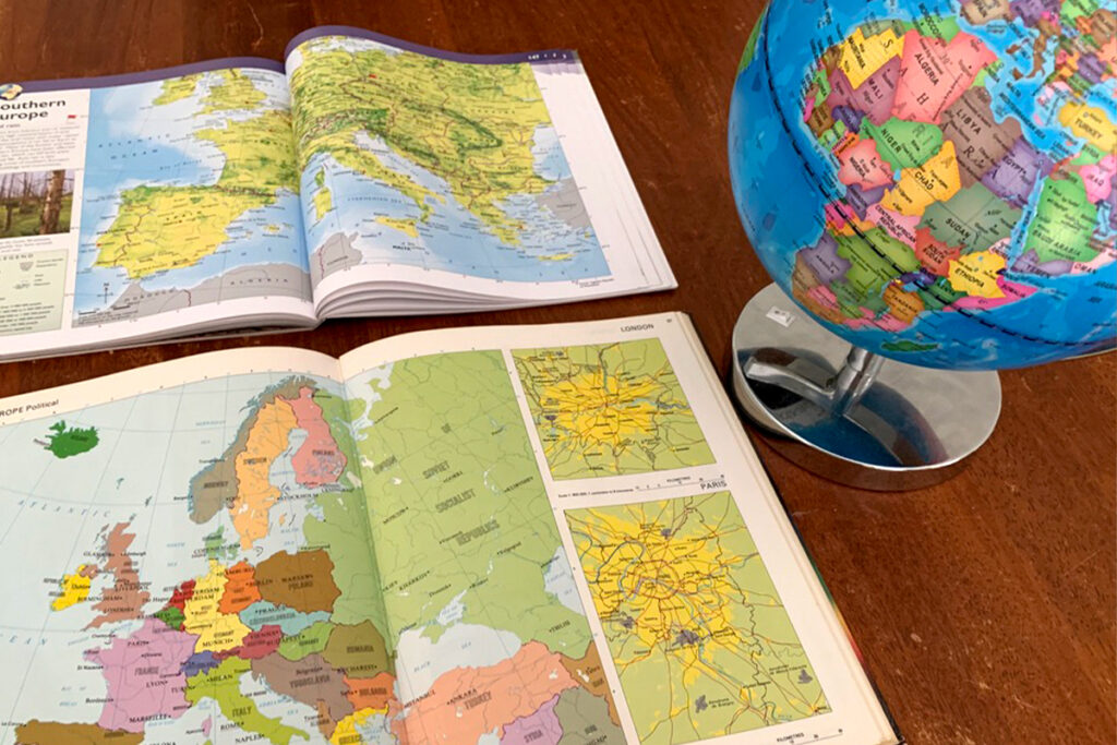 Two atlases and a globe on a wooden table used for comparing European maps. One atlas from 1982 shows countries like the USSR and Yugoslavia, while the 2024 edition displays modern borders. A colorful globe adds to the hands-on, interest-led learning setup.
