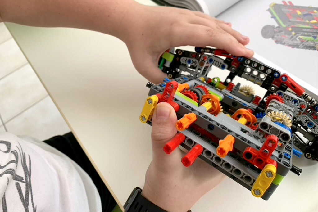 Child builds a LEGO Technic model while an instruction book sits nearby, illustrating what counts as learning in everyday life.