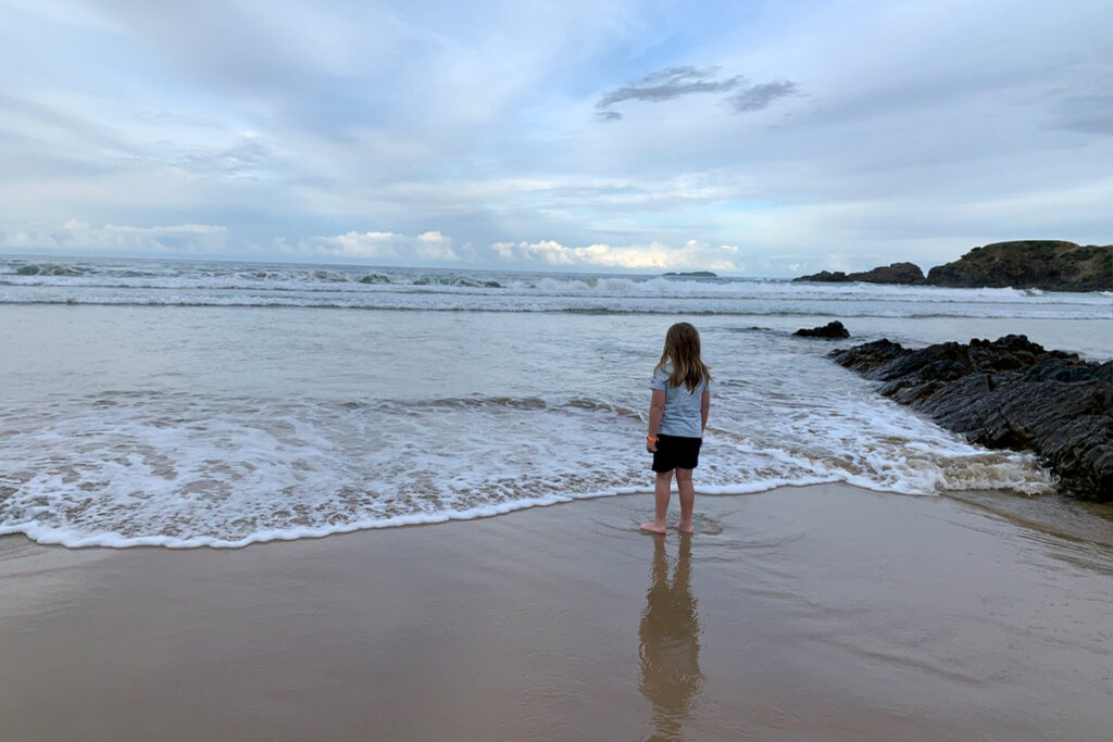 A child on a beach looking out to sea.