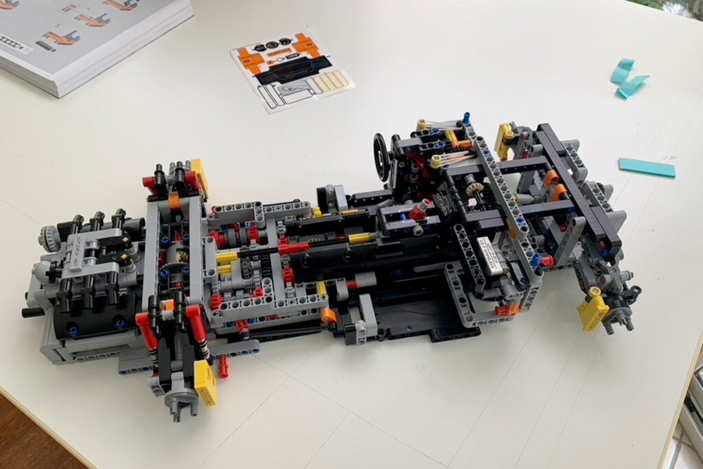 Detailed LEGO Technic style build spread across a white table with gears beams and axles visible and an instruction booklet in the corner. Photo shows interest led hands on learning while homeschooling a child with PDA through building and troubleshooting a complex model without pressure.