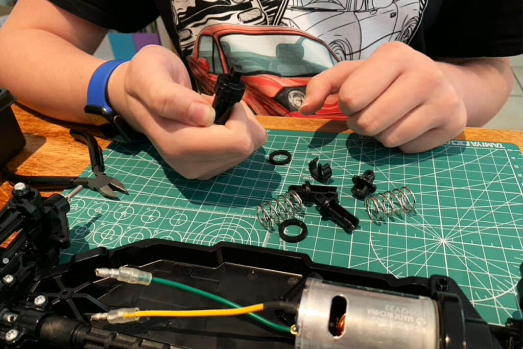 Child’s hands assembling small mechanical parts and springs on a cutting mat, with a partially built motorized model in front of them. This hands-on project highlights an alternative, engaging way to learn when a child won’t do homeschooling.